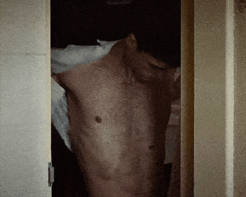 a shirtless man stands in a doorway with his eyes closed
