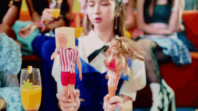 a woman is holding two dolls and a marshmallow in her hand .
