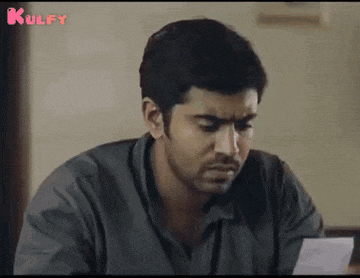 a man is sitting at a table holding a piece of paper and looking at it .