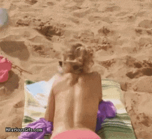 a naked woman is laying on a towel on the beach with hilariousgifs.com written on the bottom