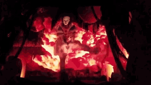 a man in a mask is standing in a room filled with flames .