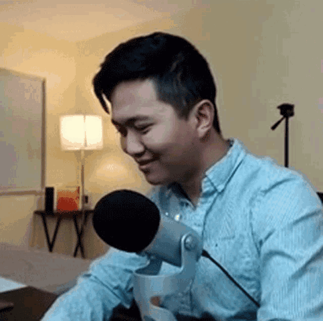 a man in a blue shirt is sitting in front of a microphone and smiling