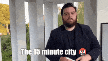 a man with a beard is holding a cell phone and says " the 15 minute city " on the bottom
