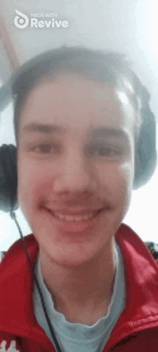 a young man wearing headphones and a red jacket is smiling at the camera .