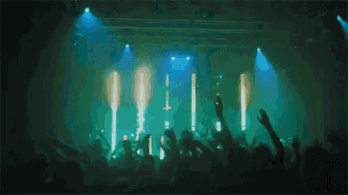 a crowd of people at a concert with their hands in the air and a blue light behind them