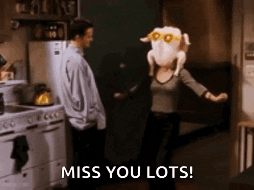 a woman is dancing in a kitchen with a stuffed turkey on her head and a man standing behind her .