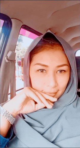 a woman wearing a hijab is sitting in a car with her hand on her chin