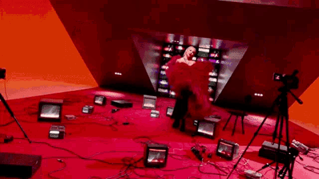 a woman in a red dress is standing in a room surrounded by televisions .