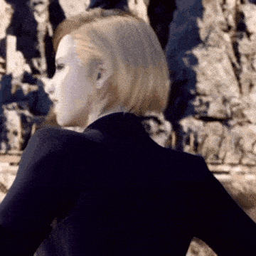 a woman in a black suit is looking over her shoulder