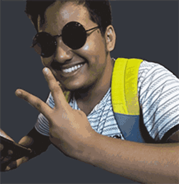 a young man wearing sunglasses and a yellow backpack is smiling
