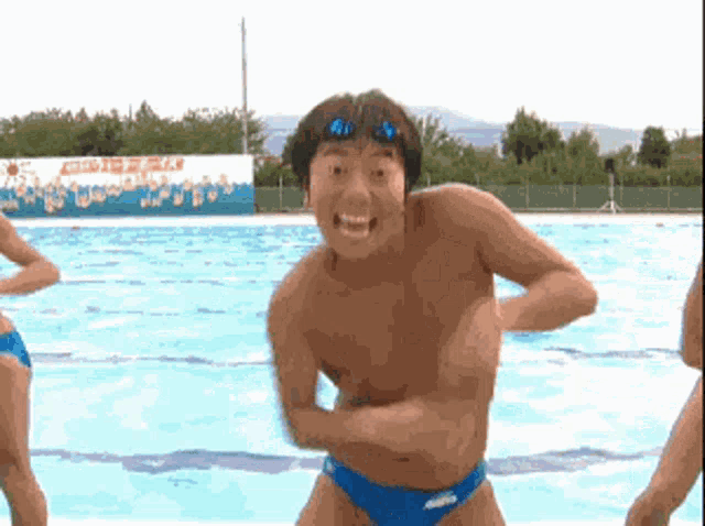 a shirtless man in blue swim trunks is standing in front of a pool