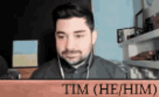 a man wearing headphones is sitting in front of a sign that says tim ( he him ) .