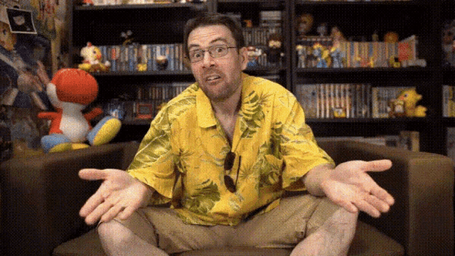 a man in a yellow shirt is sitting in front of a bookshelf with stuffed animals