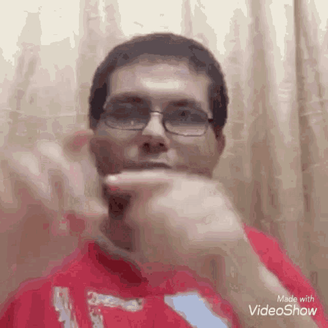 a man wearing glasses and a red shirt is making a hand gesture with his hands .