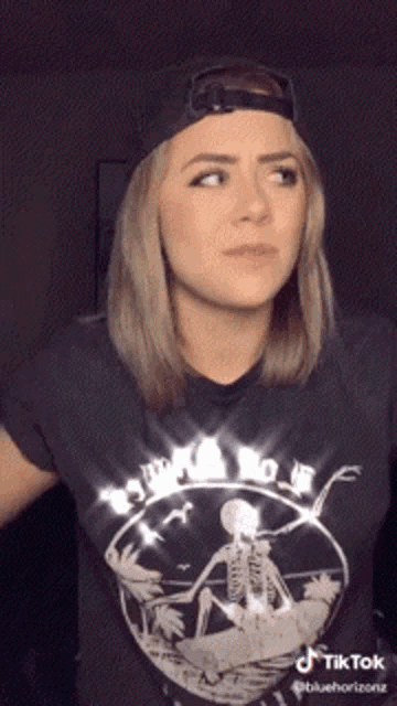 a woman wearing a black t-shirt with a skeleton on it and a hat with tiktok written on it