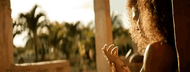 a woman with curly hair is sitting on a balcony holding a flower in her hand .