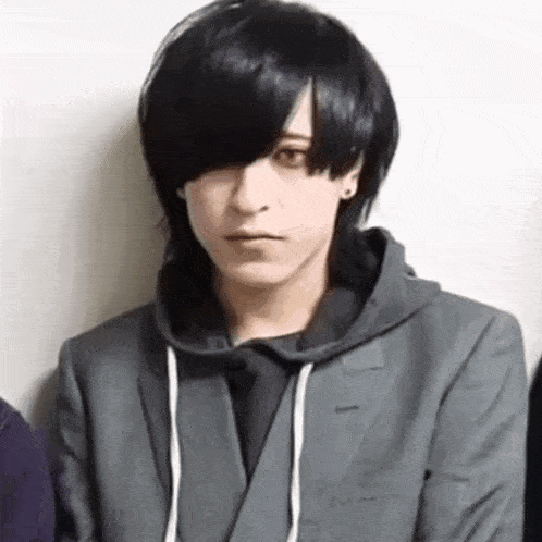 a young man with long black hair is wearing a suit and hoodie .