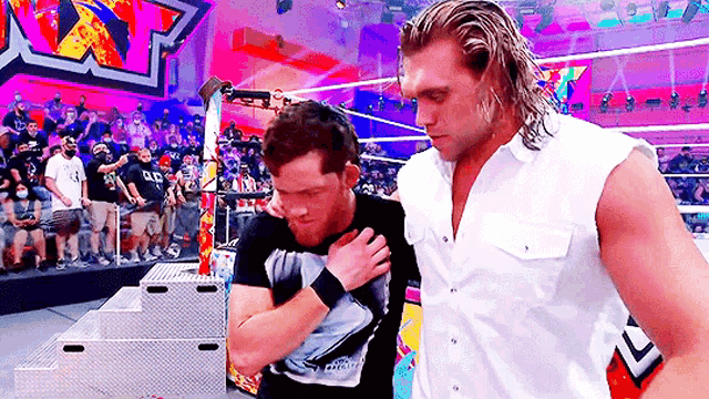 two wrestlers are standing next to each other in a wrestling ring with a crowd watching .