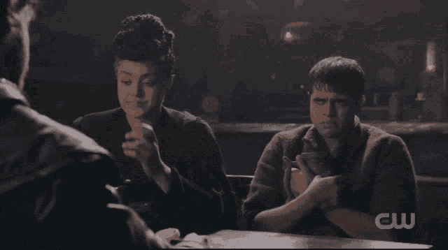 a couple of people sitting at a table with a cw logo on the bottom