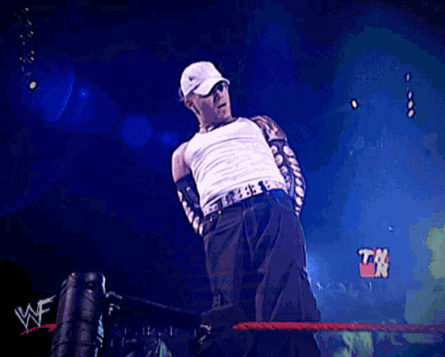 a man in a white tank top is standing in a wrestling ring with a tnt sign in the background