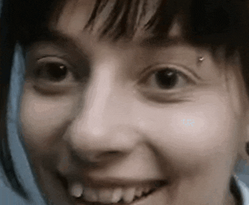 a close up of a woman 's face with a piercing in her eye and a smile .