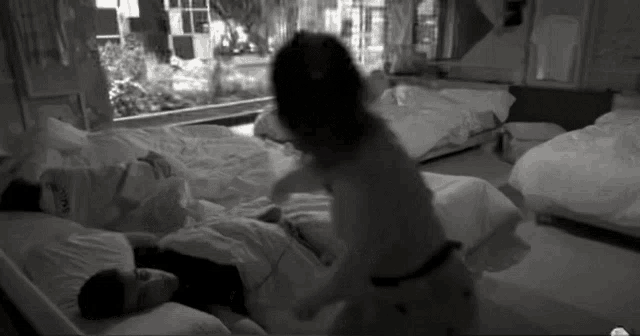 a black and white photo of a woman standing next to a man laying in bed