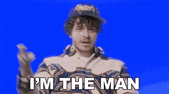 a man wearing a hat and a jacket is saying `` i 'm the man '' while holding a baseball .