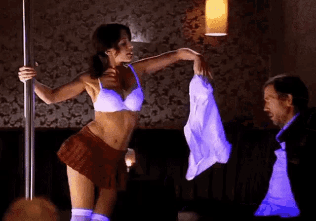 a woman in lingerie is dancing on a pole while a man holds her shirt .