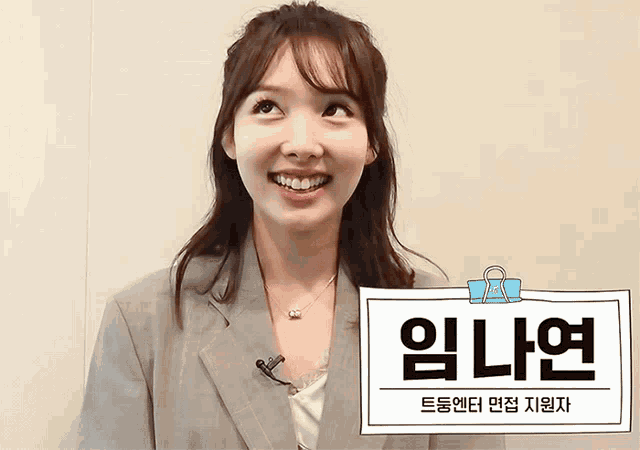 a woman in a suit is smiling while holding a sign that says ' 임 나연 ' on it