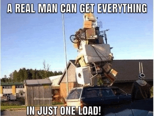 a man is standing next to a car with a pile of furniture on top of it .