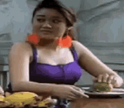 a woman in a purple tank top is sitting at a table with a plate of food on it .