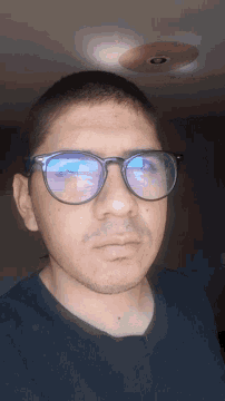 a man wearing glasses and a blue shirt looks down at something