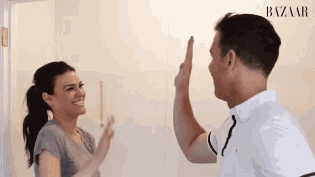 a man and woman are giving each other a high five in front of a wall that says bazaar