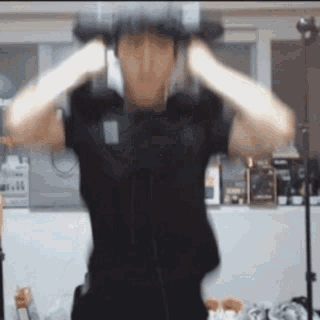 a man in a black shirt is wearing headphones and holding a dumbbell over his head .