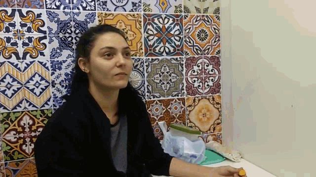 a woman sits in front of a wall with colorful tiles and looks at the camera