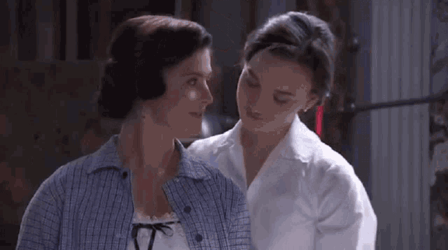 a woman with a red ribbon in her hair is kissing another woman on the cheek .