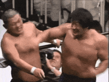 two shirtless men are fighting in a wrestling ring while a man watches .