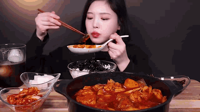 a woman is eating a bowl of food with chopsticks and a bowl of rice .