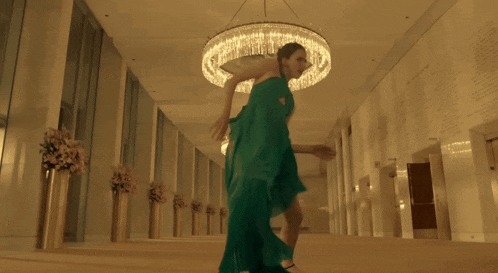 a woman in a green dress dances in a hallway
