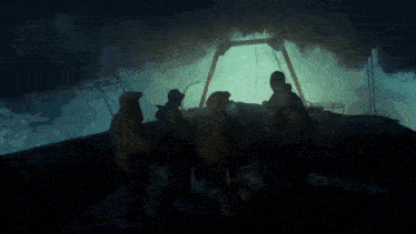 a group of people are standing on a boat in the dark with a light behind them