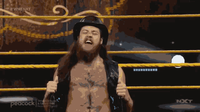 a man in a cowboy hat stands in a wrestling ring with the peacock logo in the corner