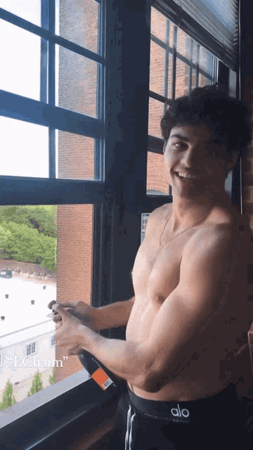 a shirtless man wearing a pair of alo shorts is standing in front of a window