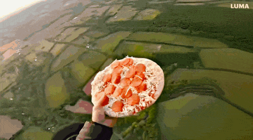 a person is holding a pizza in the air with luma written on the bottom right