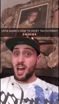 a man with a beard wearing a hat and a shirt that says gota show u how to defet teh fliters