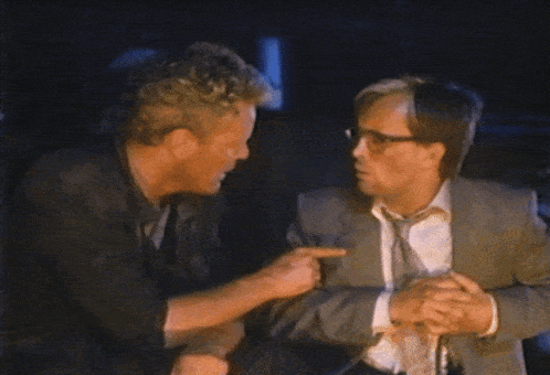 a man in a suit and tie talks to another man in a dark room