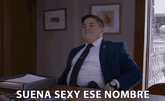 a man in a suit and tie sits at a desk with the words suena sexy ese nombre written on the bottom