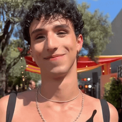 a young man with curly hair is smiling and wearing a silver necklace