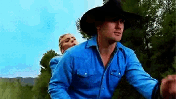 a man wearing a cowboy hat and a blue shirt is riding a horse