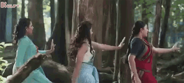 a group of women are standing in a forest holding hands .