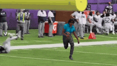 a woman is running on a football field with a gatorade cooler in the background .
